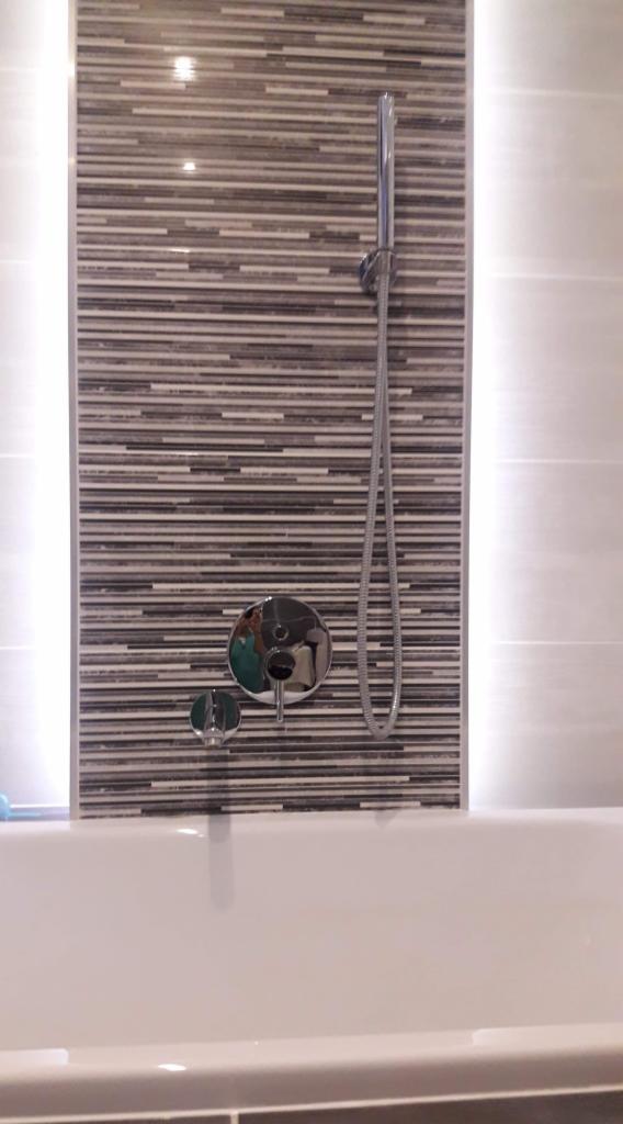 Nowoczesna łazienka: bateria wannowa z deszczownicą na tle mozaiki w odcieniach szarości, oświetlenie LED podkreślające fakturę płytek.