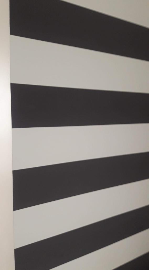 Ściana pomalowana w poziome pasy, naprzemiennie białe i grafitowe, widoczne z bliska pod kątem.