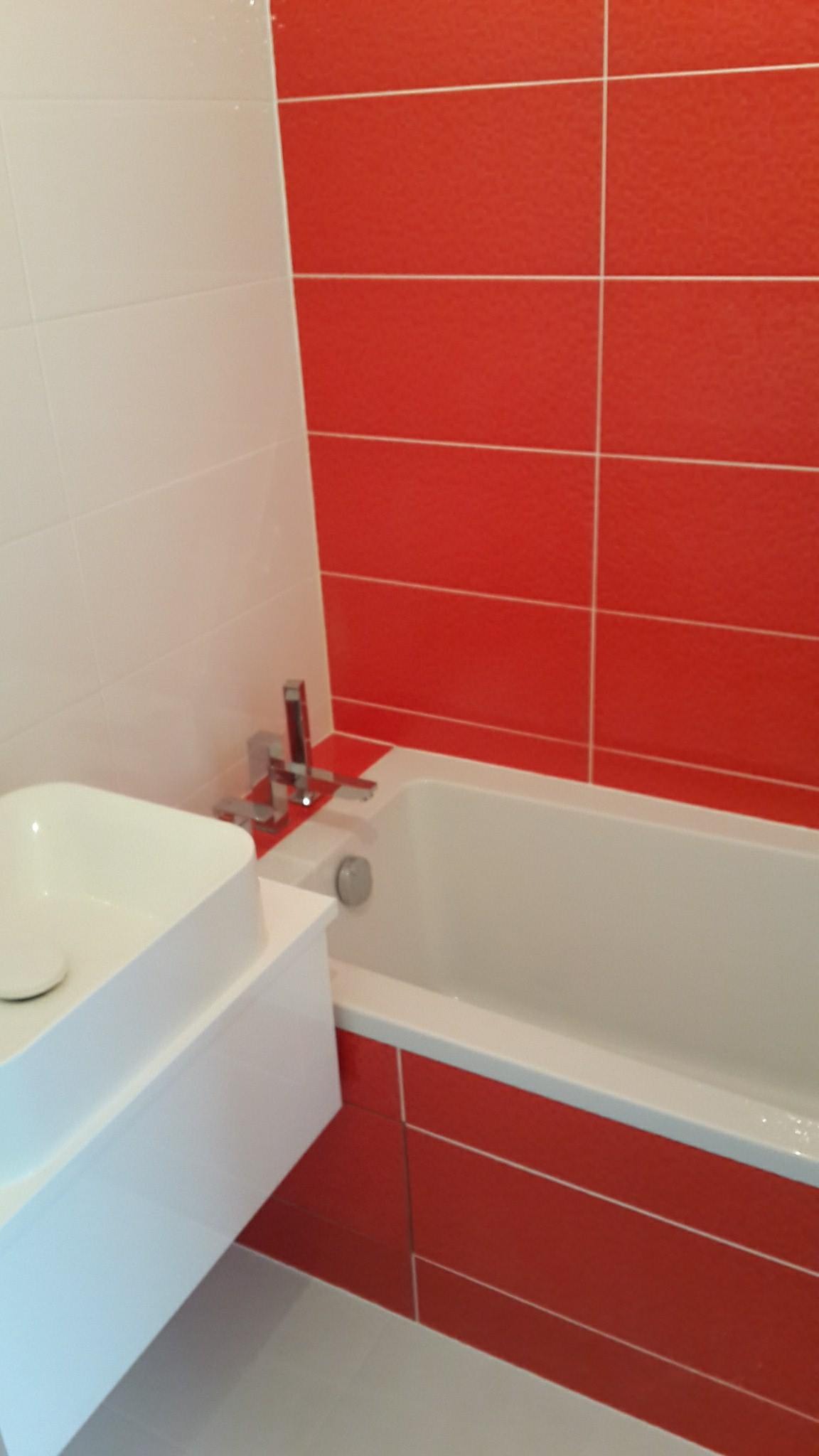 Wykończona łazienka z białą umywalką nablatową i wanną obudowaną czerwonymi płytkami, uzupełniona białymi płytkami na ścianie.
