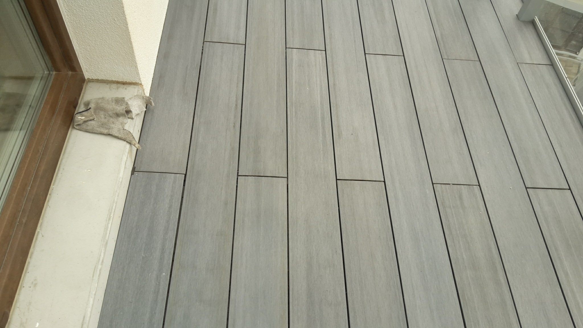 Szare deski tarasowe kompozytowe ułożone na balkonie, widoczna szmatka przy framudze okna.