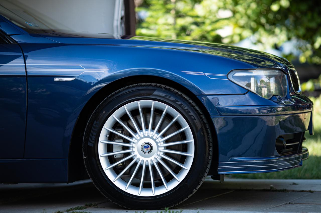 Fragment niebieskiego samochodu marki Alpina z charakterystycznymi srebrnymi felgami i paskami dekoracyjnymi, opona Pirelli P Zero.