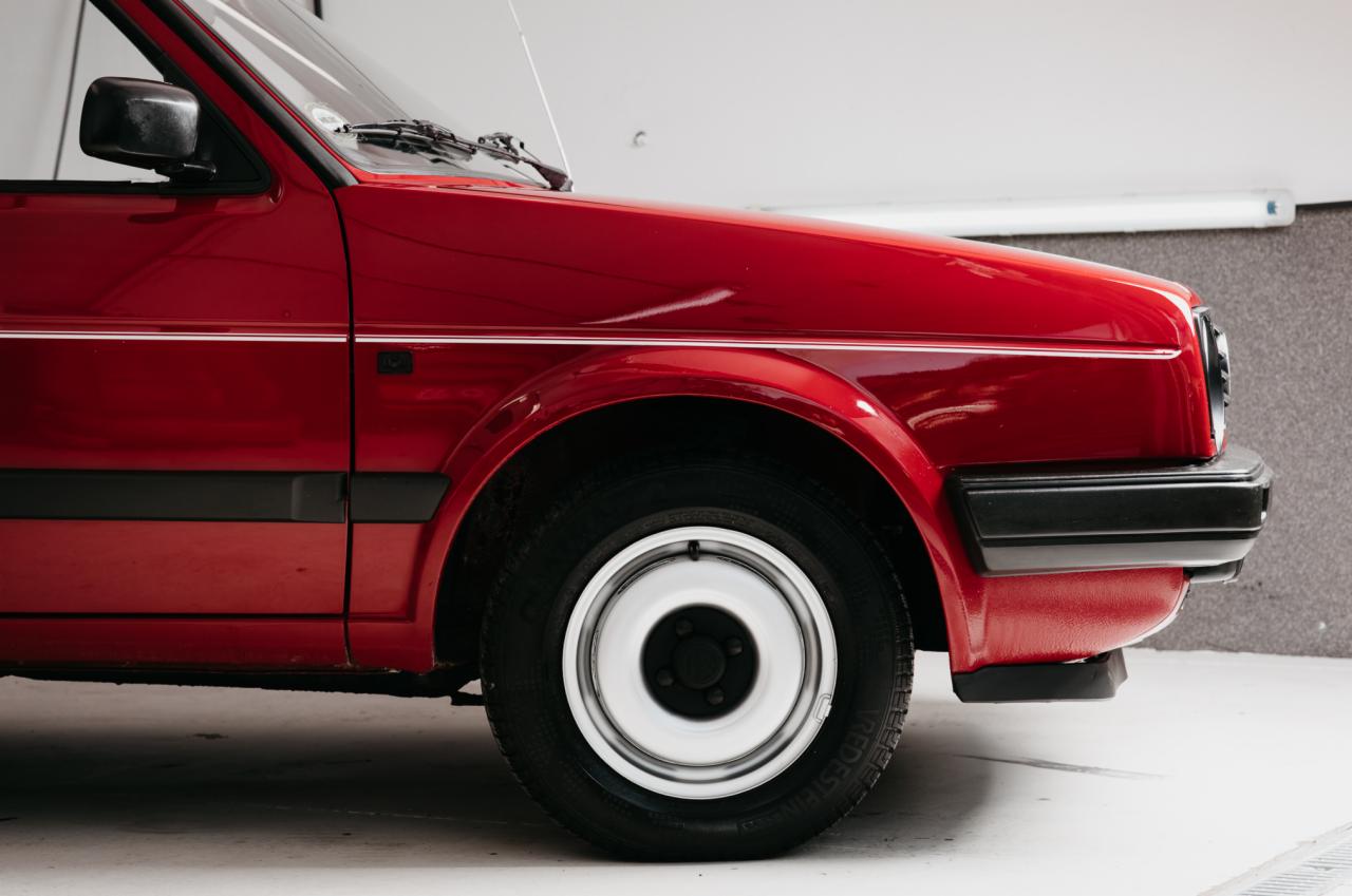 Czerwony samochód osobowy, widok z boku na przednie koło i fragment karoserii, z widocznymi detalami takimi jak biała listwa i opony Vredestein.