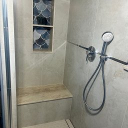 Usługi remontowo-budowlane - Stylowa kabina prysznicowa z półką wnękową wykończoną mozaiką w odcieniach niebieskiego. Jasne płytki imitujące kamień, siedzisko i heksagonalna podłoga.