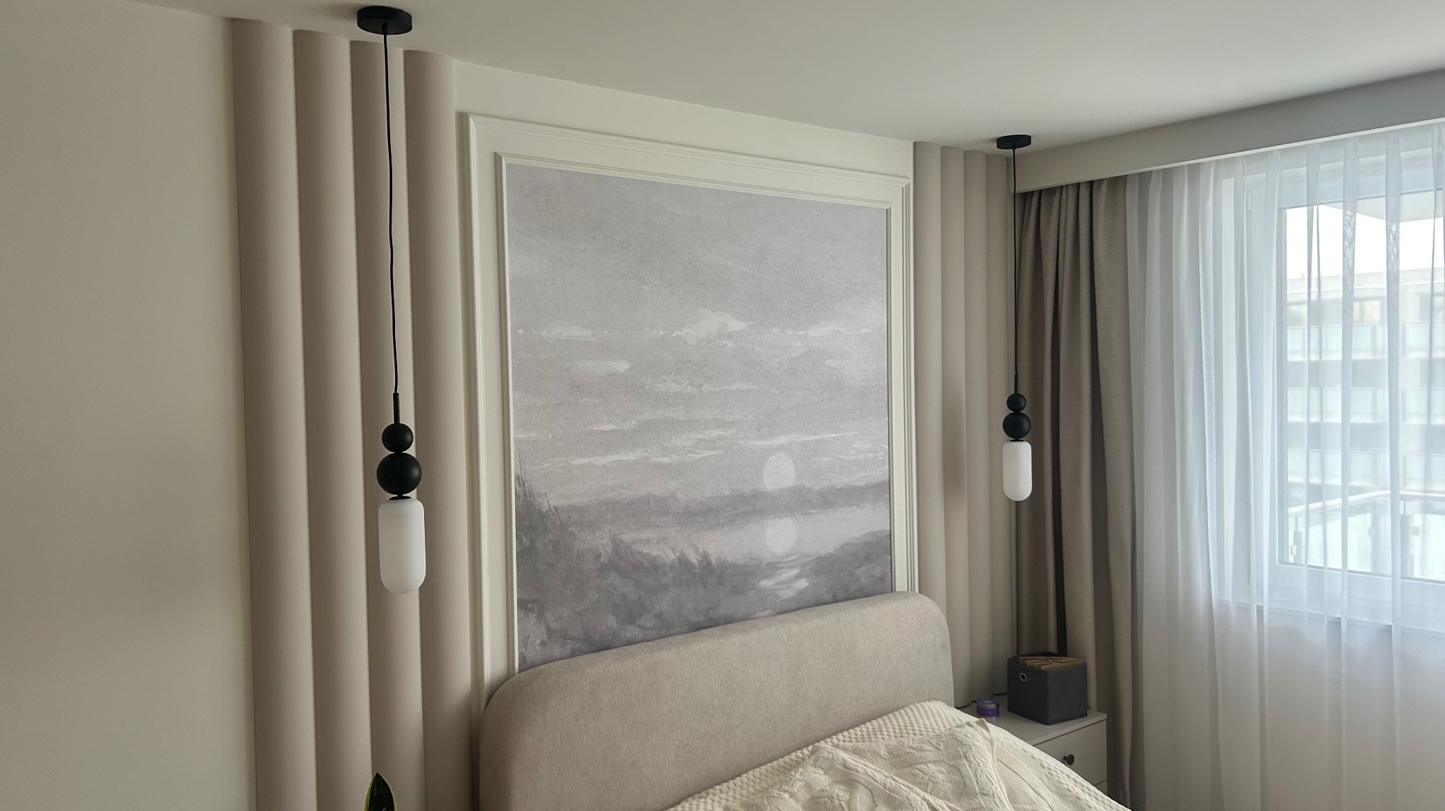 Elegancka sypialnia z beżowymi panelami ściennymi, obrazem w ramie nad łóżkiem i wiszącymi lampami. Okno z firankami w tle.