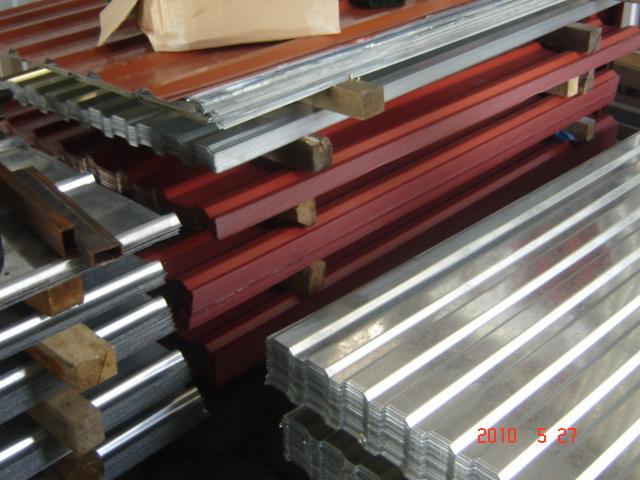 Stos arkuszy blachy trapezowej w kolorze srebrnym i ceglastym, ułożonych na drewnianych legarach, widoczne ślady korozji i zabrudzenia.