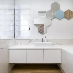 Nowoczesna łazienka z białymi szafkami pod umywalką, heksagonalnymi lustrami i drewnianymi akcentami na ścianie oraz podłodze.
