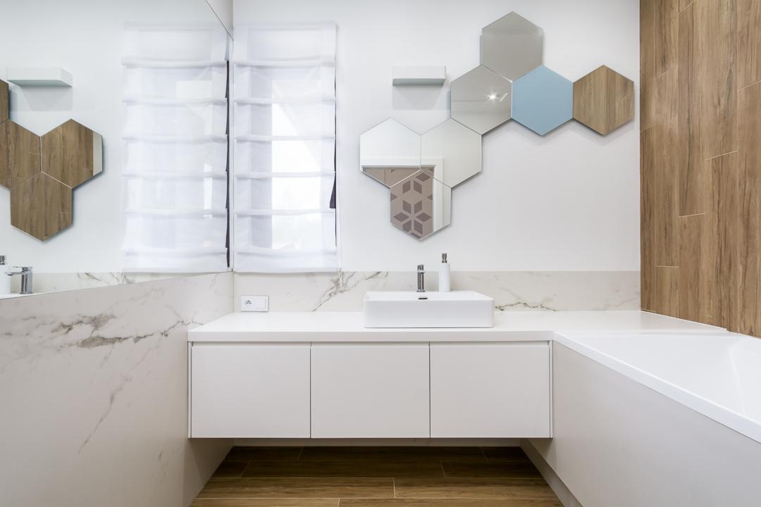 Nowoczesna łazienka z białymi szafkami pod umywalką, heksagonalnymi lustrami i drewnianymi akcentami na ścianie oraz podłodze.