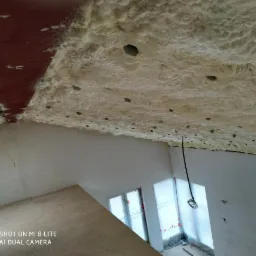 Poddasze po natrysku pianki izolacyjnej, widoczne otwory wentylacyjne, surowe ściany i okna zabezpieczone folią.