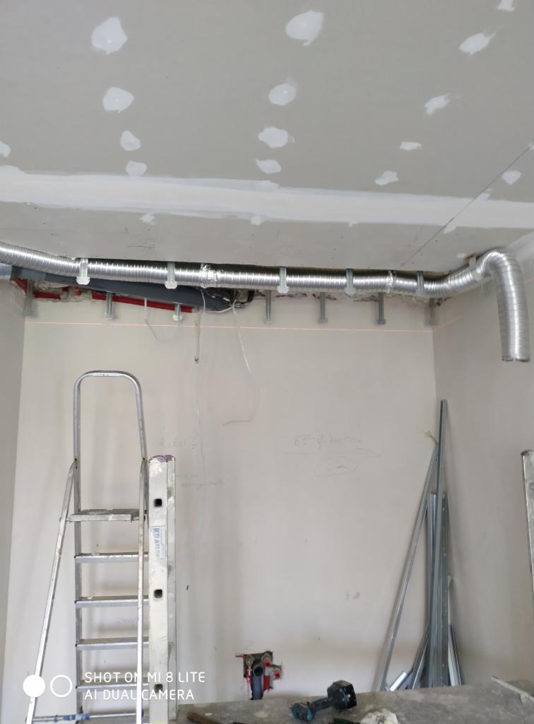 Montaż elastycznego przewodu wentylacyjnego pod sufitem z płyt kartonowo-gipsowych, widoczna drabina i laserowy poziom