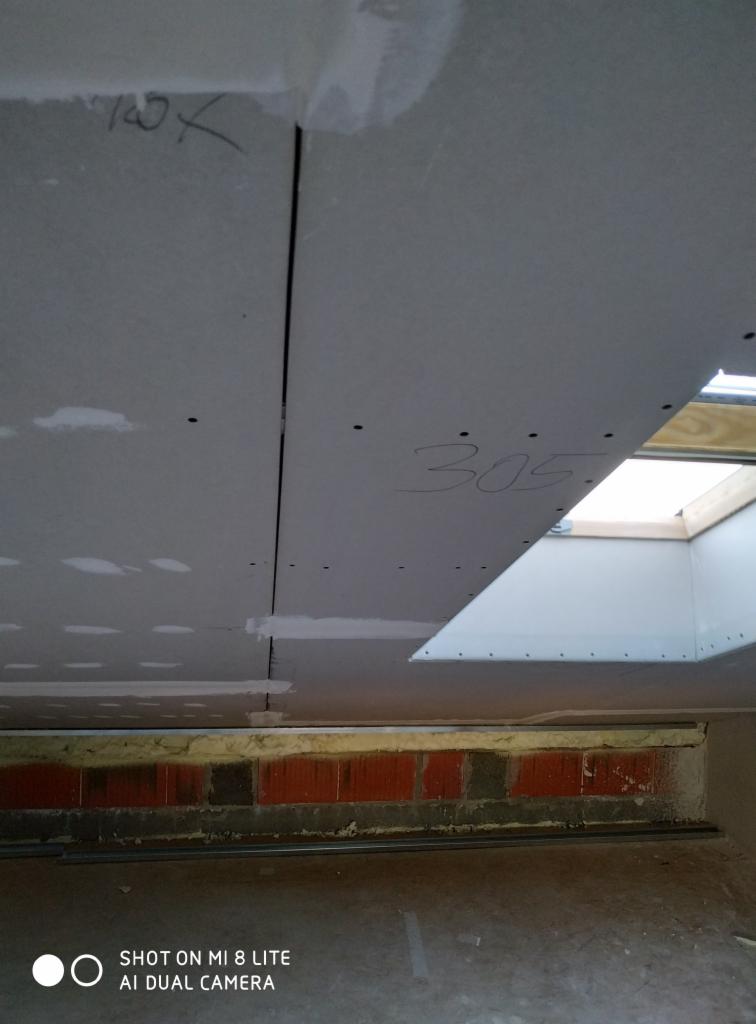 Montaż sufitu podwieszanego z widocznymi łączeniami płyt, numerem 305 napisanym odręcznie i oknem dachowym w tle.