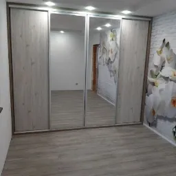 Czterodrzwiowa szafa przesuwna z lustrami, drewnopodobne fronty, widoczna fototapeta z motywem kwiatowym na ścianie.