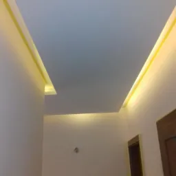 Podwieszany sufit z oświetleniem LED wzdłuż krawędzi, widok z dołu, widoczne fragmenty dwóch ścian i ościeżnica drzwi.