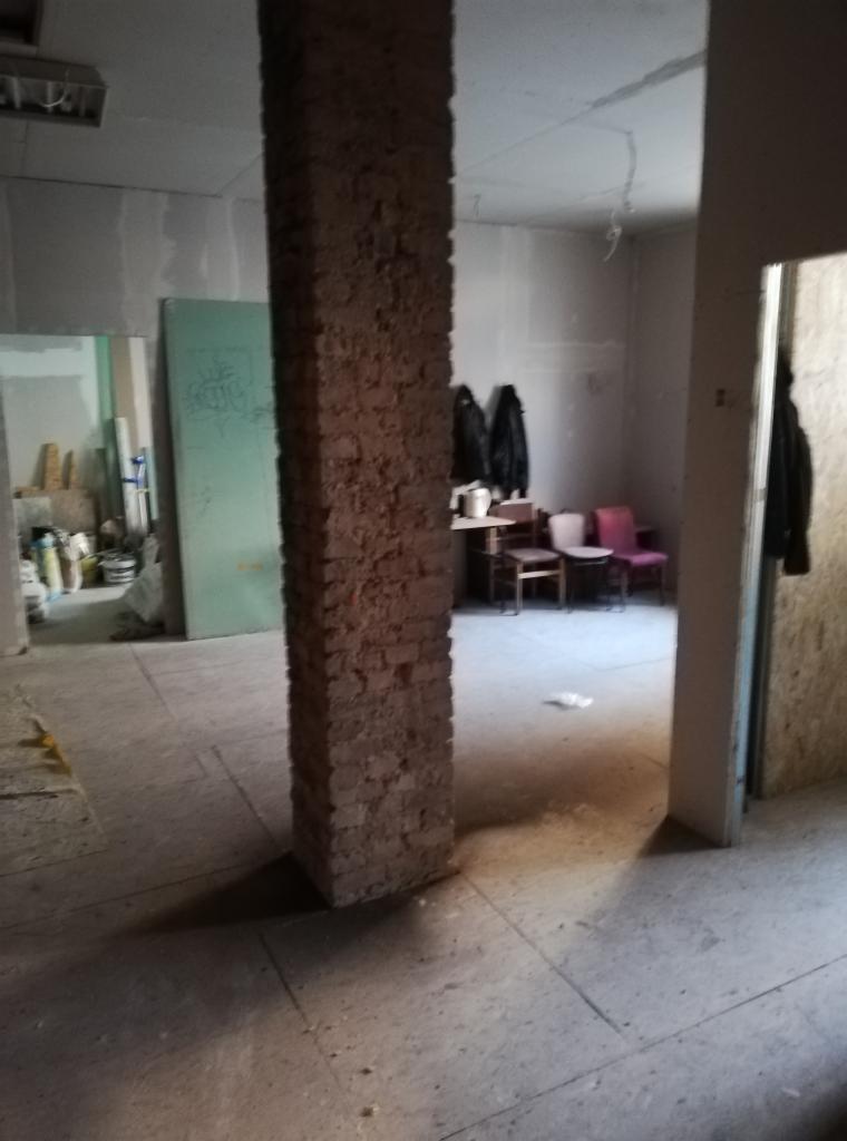 Surowa ceglana kolumna w surowym wnętrzu w trakcie remontu, widoczne ślady po tynku, szpachli i gładzi, w tle drzwi z resztkami farby i umeblowanie