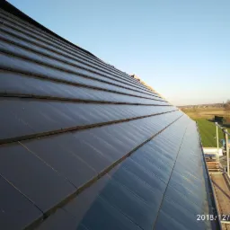 Nowe, błyszczące, grafitowe dachówki ceramiczne ułożone na dachu domu jednorodzinnego, widok z rusztowania w słoneczny dzień.