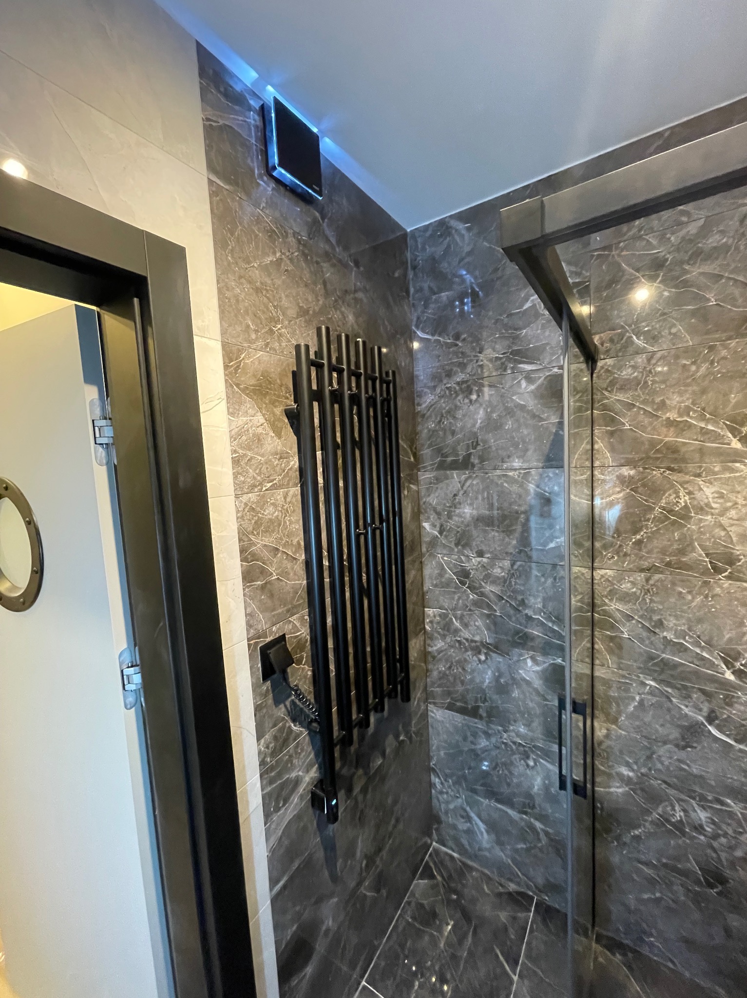 Wykończona łazienka z marmurowymi płytkami, czarnym grzejnikiem drabinkowym i kabiną prysznicową z czarnymi ramami. Nowoczesny design z oświetleniem LED.