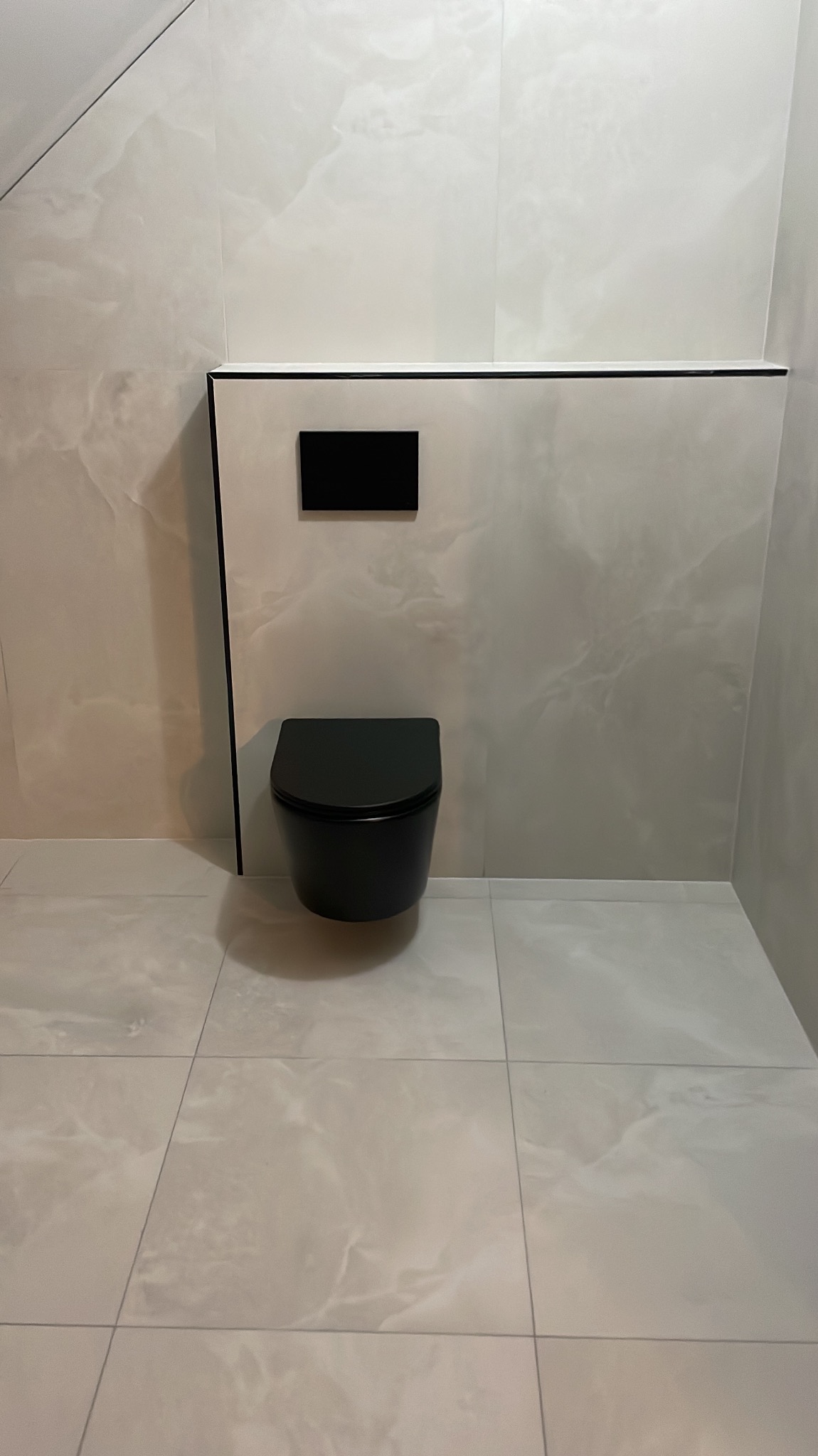 Wykończona łazienka z podwieszaną, czarną toaletą na tle marmurowych płytek w odcieniach szarości. Minimalistyczny design z czarnymi akcentami.