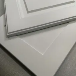 Dwa białe fronty szafek z frezowanymi ramkami, jeden na drugim, widoczne z bliska pod kątem.