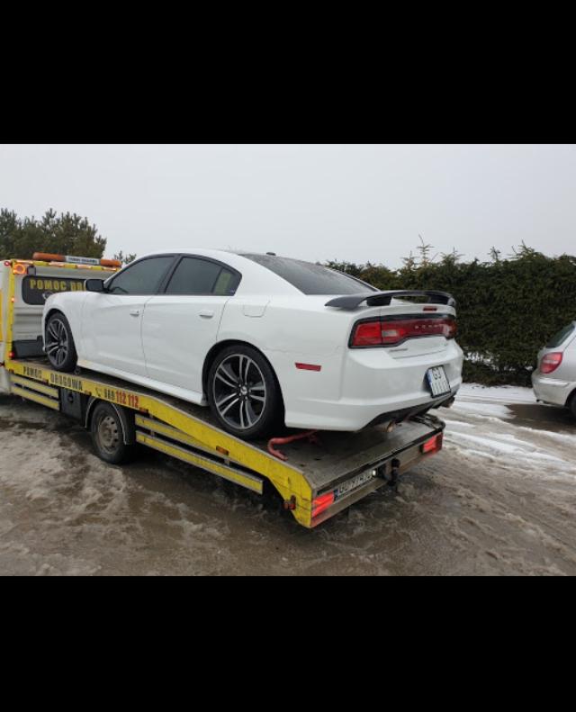 Biały samochód osobowy Dodge Charger na żółtej platformie pojazdu pomocy drogowej w zimowej scenerii.