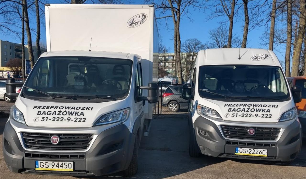 Dwa białe busy Fiat Ducato z napisem 'Przeprowadzki Bagażówka' i numerem telefonu, zaparkowane obok siebie na parkingu w słoneczny dzień.