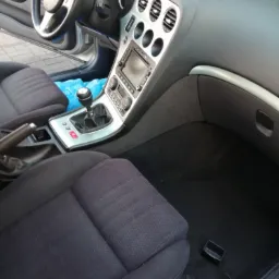 Wnętrze samochodu Alfa Romeo z widocznymi czarnymi, tekstylnymi fotelami, deską rozdzielczą w kolorze czarnym i srebrnym oraz elementami sterowania. Na podłodze widoczne drobne śmieci i plastikowy...