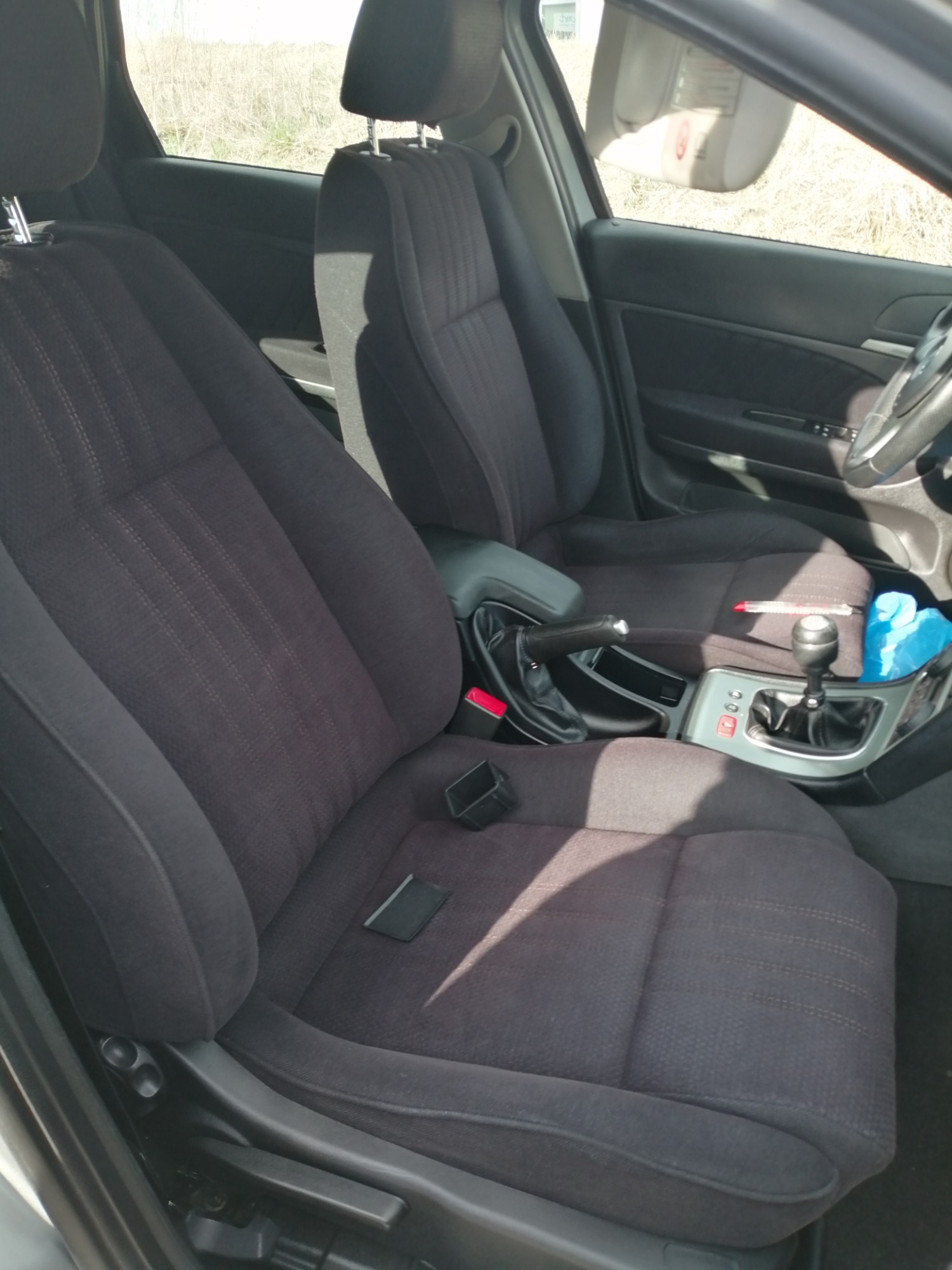 Wnętrze samochodu Alfa Romeo z ciemną tapicerką materiałową przednich foteli, widoczny tunel środkowy z dźwignią zmiany biegów i hamulcem ręcznym, częściowo widoczna kierownica i deska rozdzielcza.