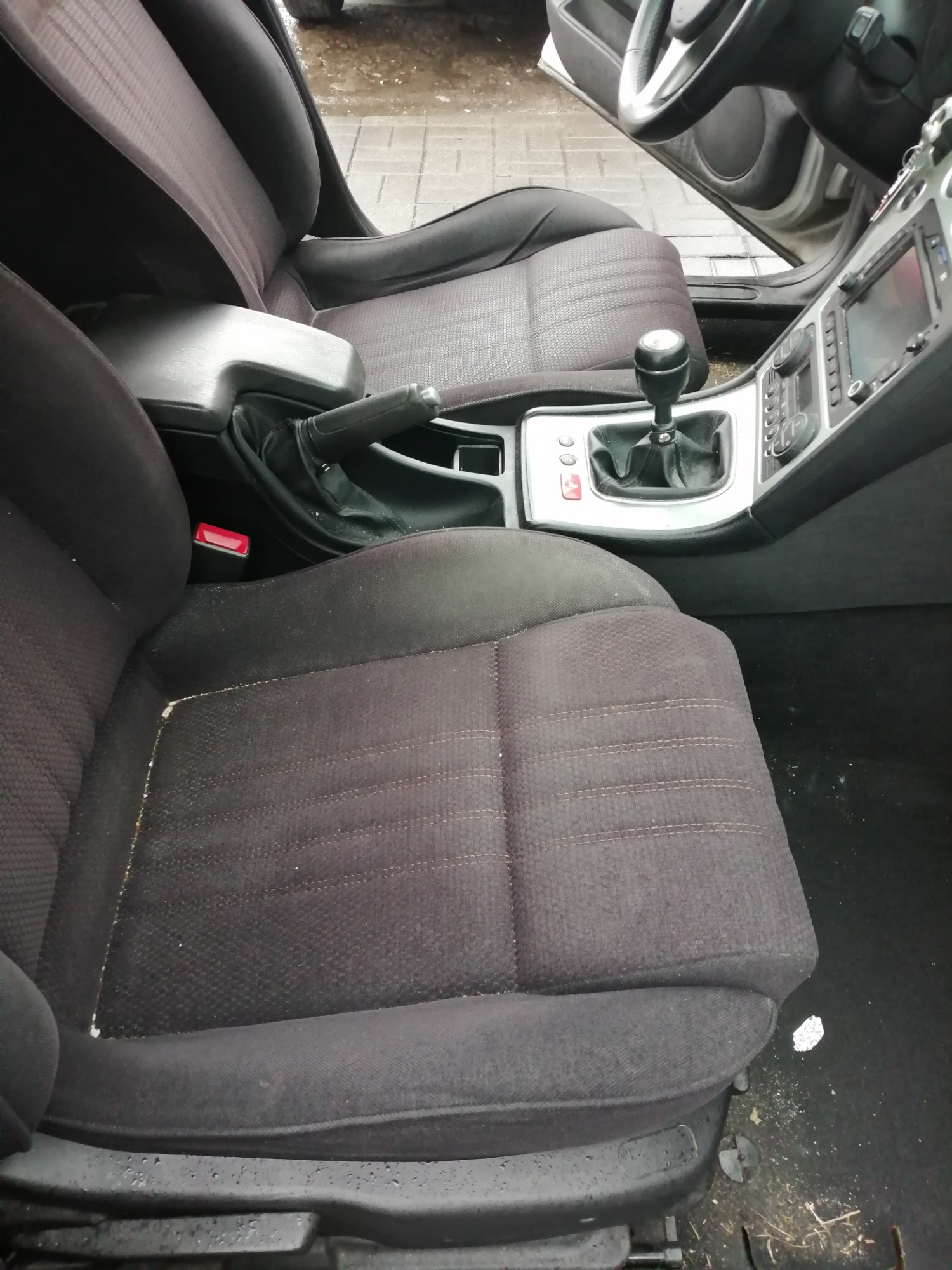 Brudne, czarne fotele samochodowe z widocznymi okruchami i śladami użytkowania, wnętrze Alfa Romeo 159 przed czyszczeniem.