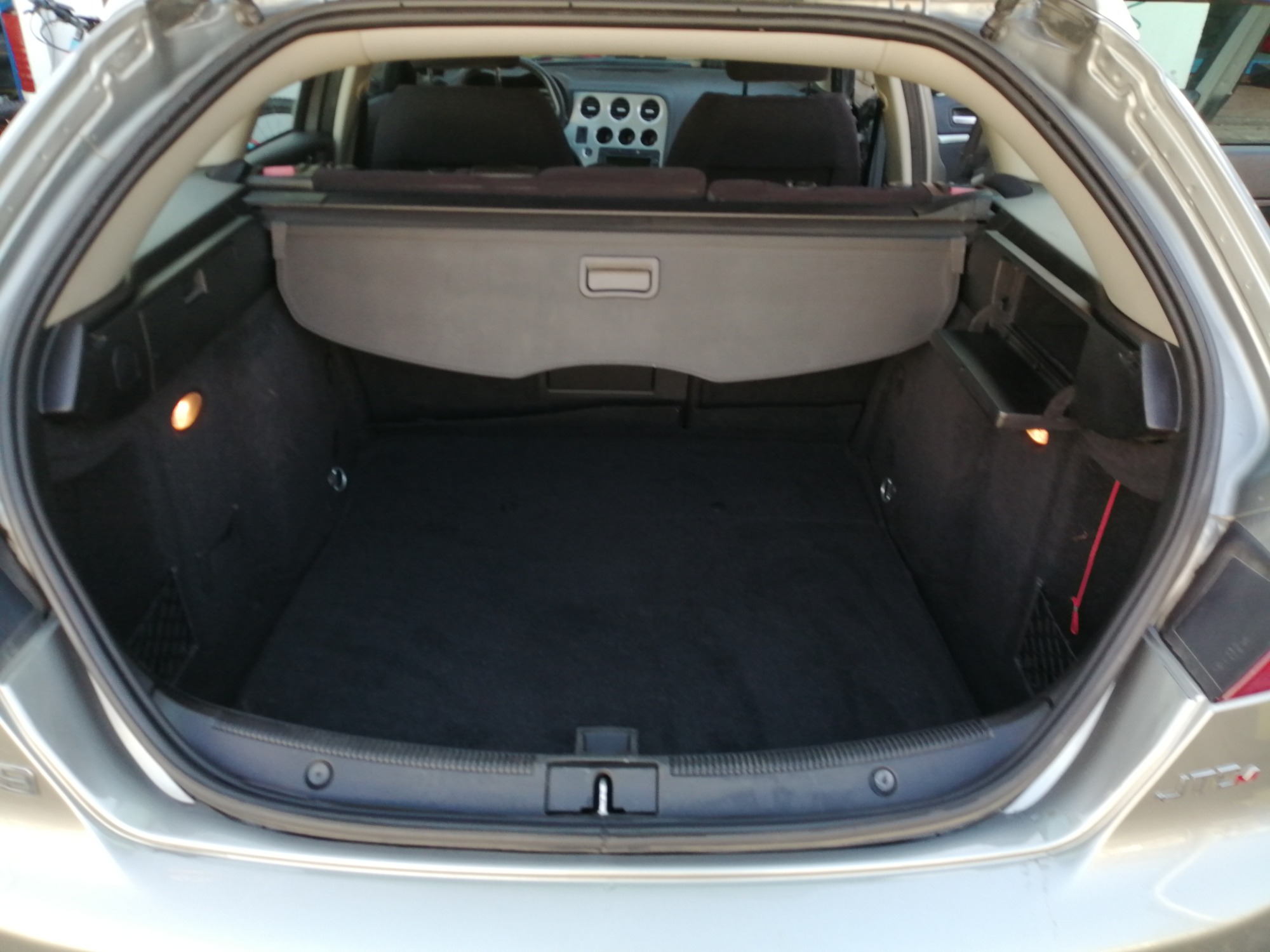 Wnętrze bagażnika samochodu typu hatchback, widoczna czarna tapicerka, roleta bagażnika w kolorze szarym i oświetlenie boczne.