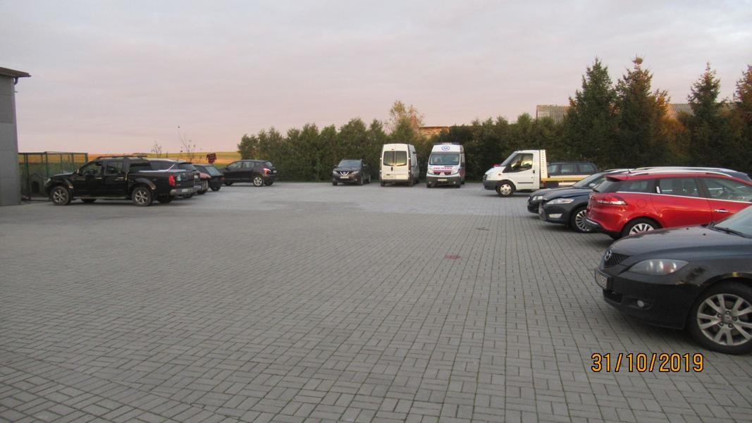 Parking przed serwisem samochodowym w Szczecinku, z widocznymi samochodami osobowymi i dostawczymi, w tym pojazd z oznaczeniami serwisu likwidacji szkód.