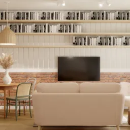 Jasny salon z ceglaną ścianą, drewnianym stołem i krzesłami, beżową sofą i półkami z książkami pod sufitem, oświetlony lampą z wikliny.