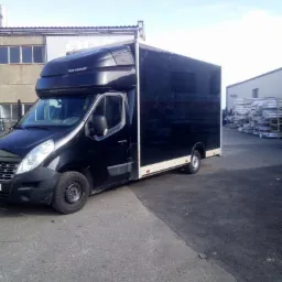 Czarny bus transportowy 'Pony Fantasy' zaparkowany na szarym asfalcie, z budynkami w tle i stertą metalowych profili.