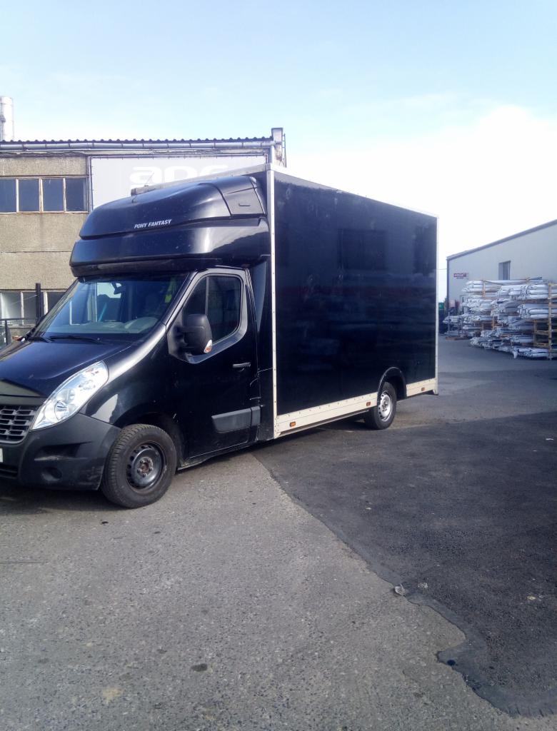 Czarny bus transportowy 'Pony Fantasy' zaparkowany na szarym asfalcie, z budynkami w tle i stertą metalowych profili.