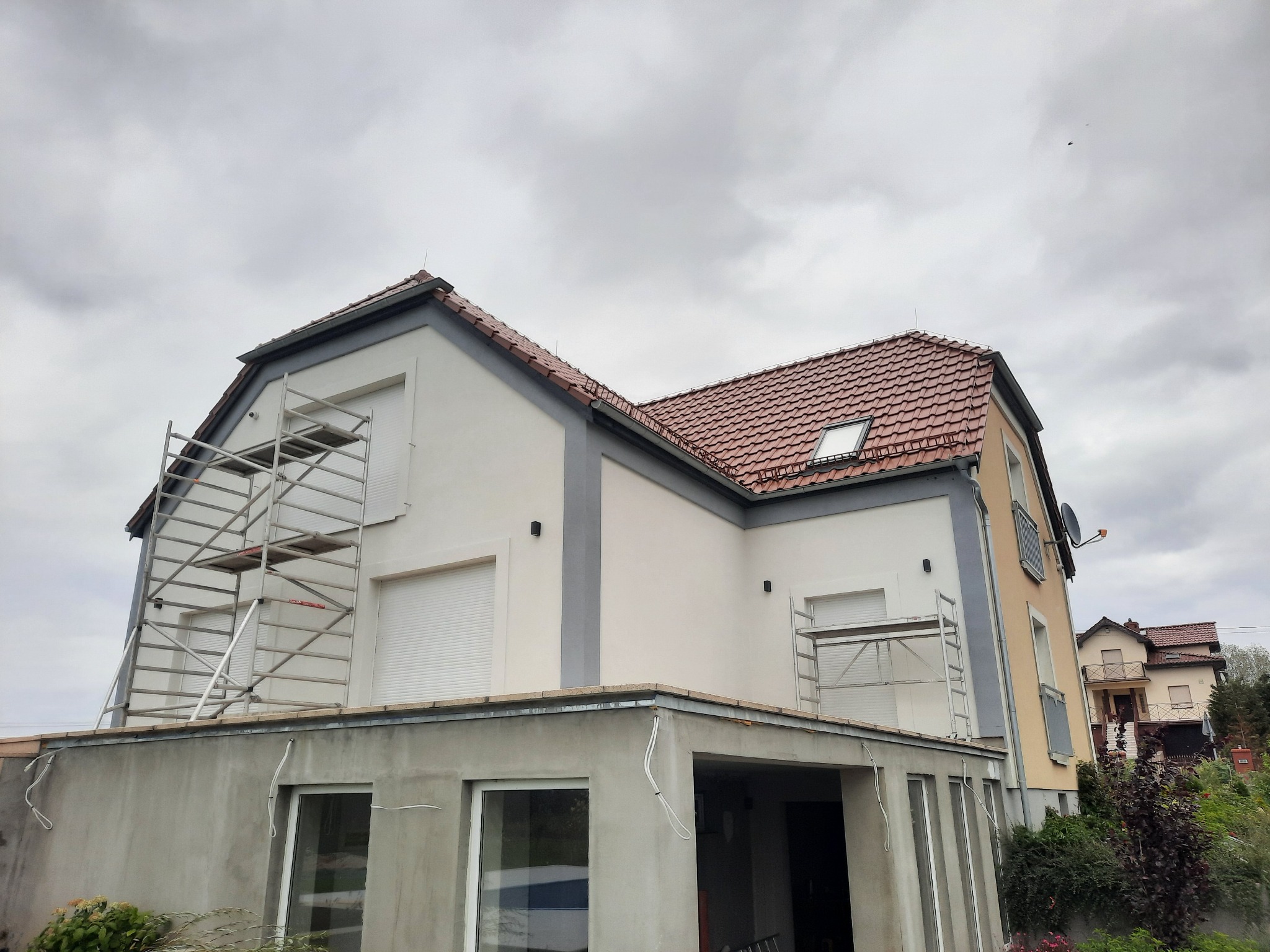 Dom jednorodzinny z częściowo ocieploną elewacją, widoczne rusztowania i niedokończona dobudówka.