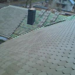 Montaż gontu bitumicznego na dachu, widoczny komin z cegły, przygotowane łaty i wstępne ułożenie gontów przed ostatecznym montażem.