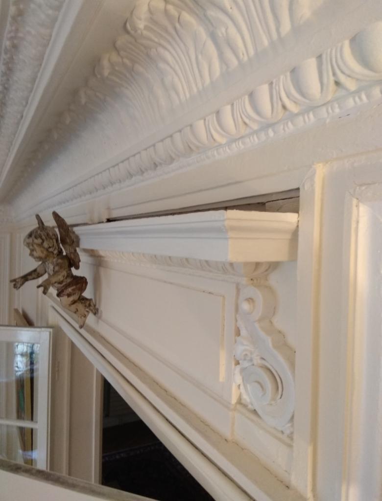 Detal dekoracyjny: biała sztukateria na suficie i ścianie z ornamentami roślinnymi oraz figurką aniołka, widoczne ślady niedokładnego wykończenia.