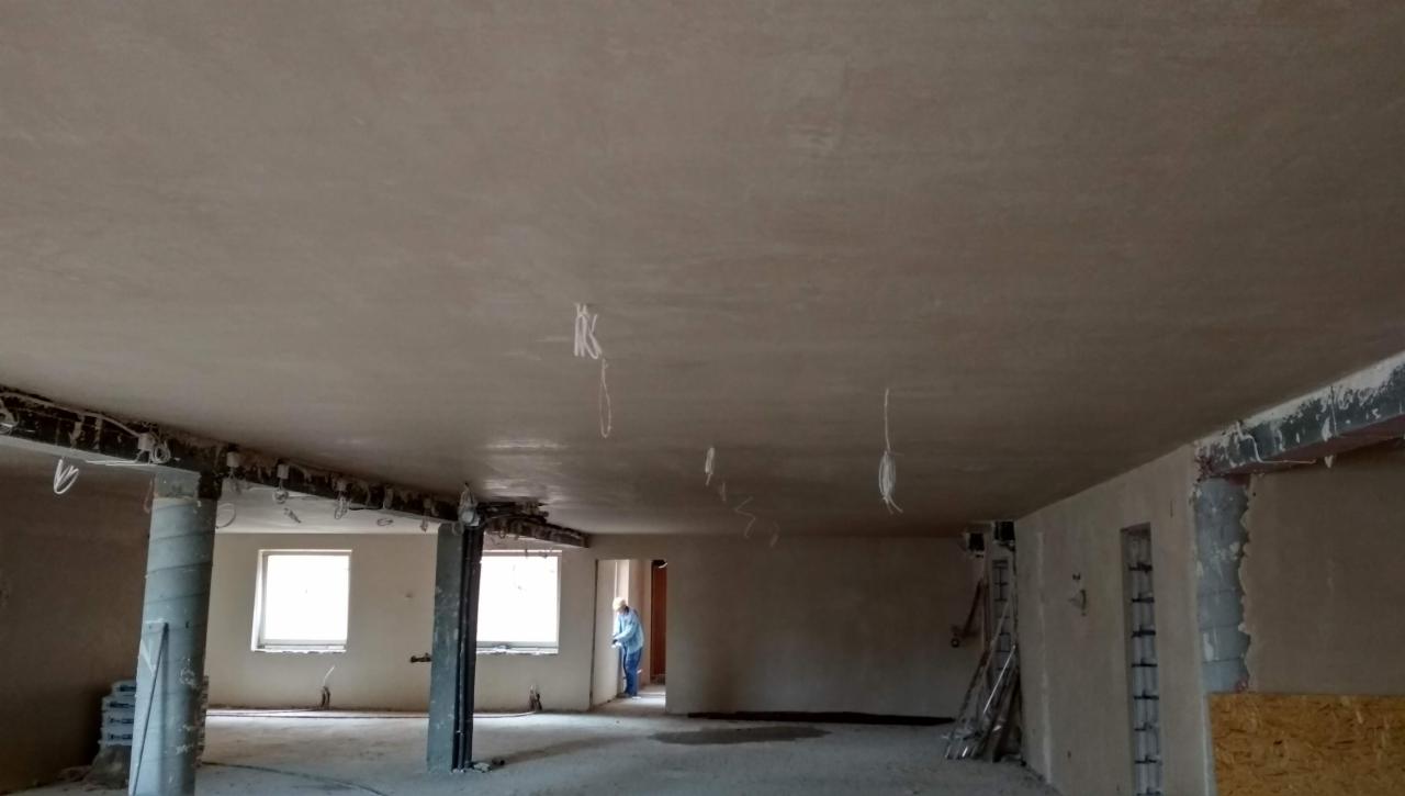 Świeżo położone tynki maszynowe na suficie w przestronnym, jasnym pomieszczeniu w trakcie remontu, z widocznymi przewodami i elementami konstrukcyjnymi.