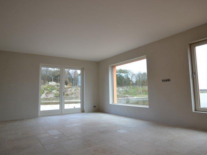 Wnętrze świeżo wykończonego pokoju z jasnymi, gładkimi ścianami, widocznymi oknami z widokiem na zewnątrz i kamienną podłogą z regularnym wzorem kwadratów.