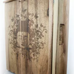 Drewniana szafka z grawerowanym motywem Buddy, kwiatów i motyli, widoczne zawiasy i uchwyt.