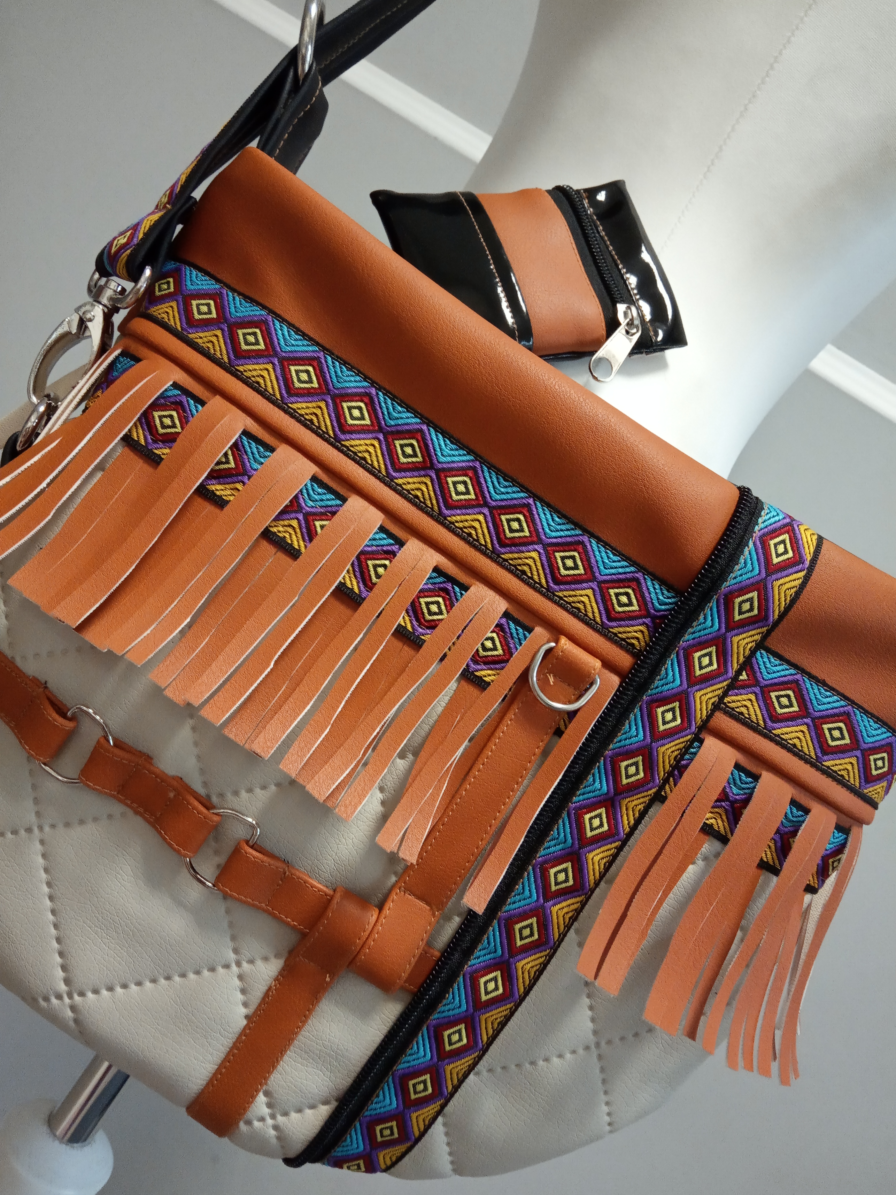 Torba damska z brązowej i białej skóry ekologicznej, zdobiona kolorowym etnicznym wzorem i frędzlami, z dopasowaną portmonetką na suwak, prezentowana na manekinie.