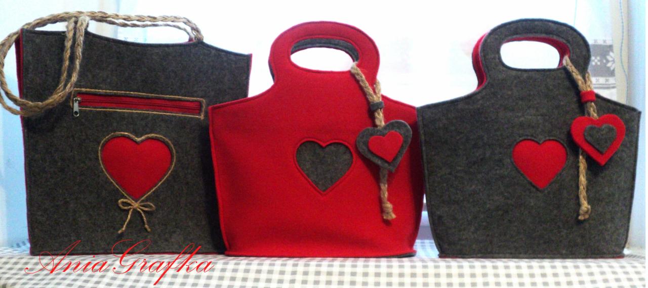 Trzy filcowe torby: szara z czerwoną kieszenią na zamek i aplikacją serca związaną sznurkiem, czerwona z wyciętym szarym sercem i zawieszką serca na sznurku, oraz szara z czerwoną aplikacją serca...