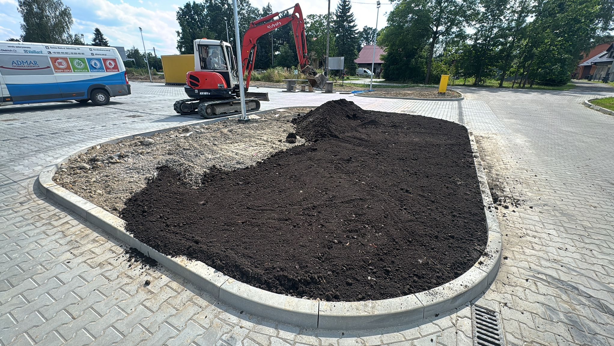 Kształtowanie terenu pod rabatę z ziemią ogrodową, widoczny mini-koparka Kubota KX161-3 na kostce brukowej. Obrzeże rabaty wykończone betonowym krawężnikiem.