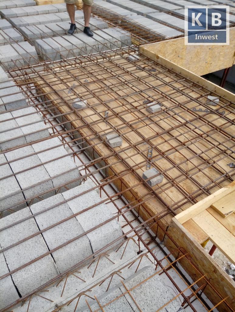 Wiązanie zbrojenia na stropie z pustaków szalunkowych, widoczny fragment konstrukcji szalunkowej i logo KB Invest w prawym górnym rogu.