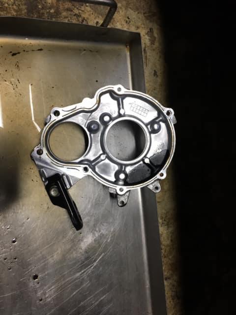 Oczyszczona, aluminiowa obudowa pompy oleju silnika samochodowego, leżąca na metalowej tacy warsztatowej, widoczne ślady oleju.