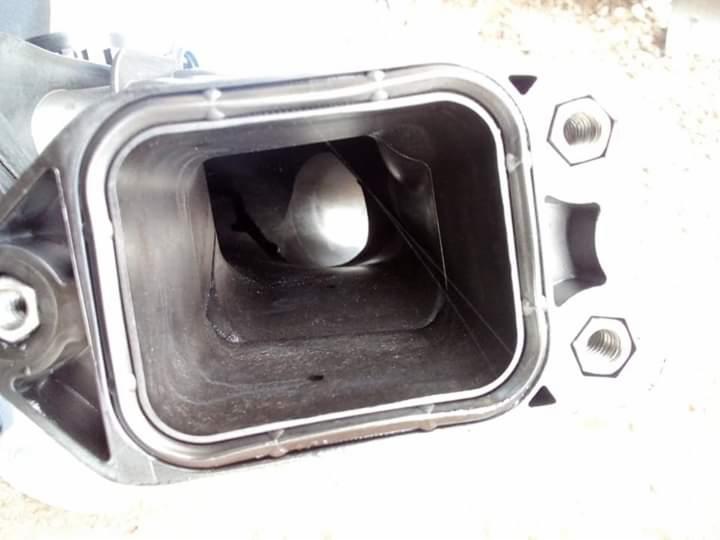 Wnętrze kolektora dolotowego silnika spalinowego, widok od strony przepustnicy, z widocznymi śladami użytkowania i gwintowanymi otworami montażowymi.