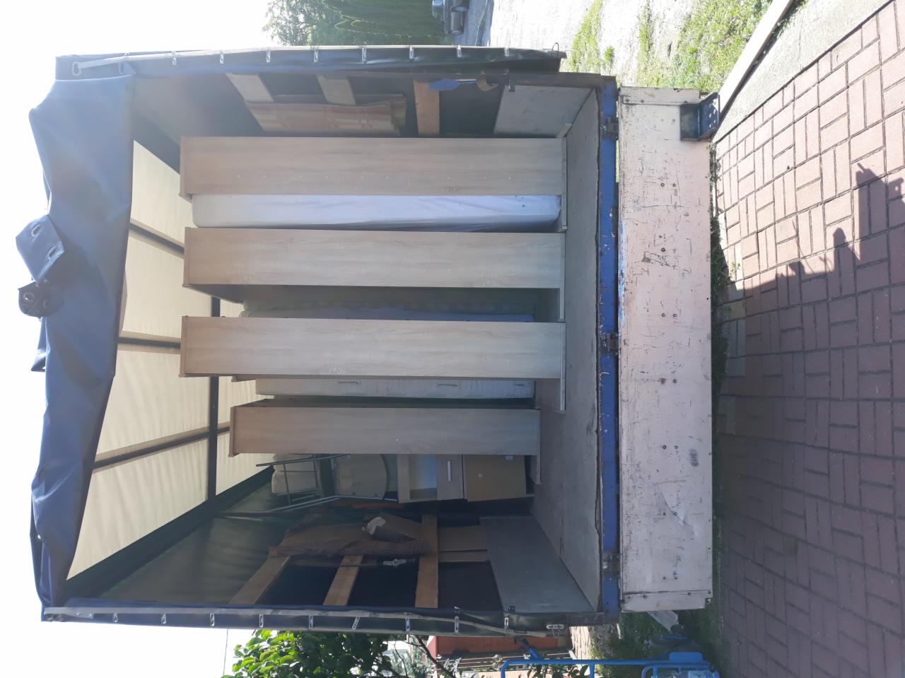 Wnętrze samochodu dostawczego z plandeką, wypełnione meblami podczas transportu, widoczne komody z szufladami i materac.