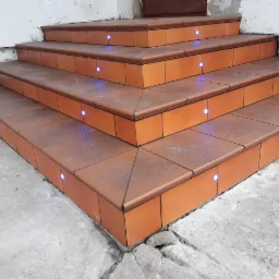 Zewnętrzne schody wejściowe wyłożone terakotą z wbudowanym oświetleniem LED, widoczne pęknięcia w betonie u podstawy.