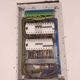 MK-INSTAL Michał Kaczmarski - Rozdzielnica elektryczna Schneider zamontowana we wnęce ściany, widoczne zabezpieczenia i przewody w kolorach: niebieskim, brązowym, żółto-zielonym.