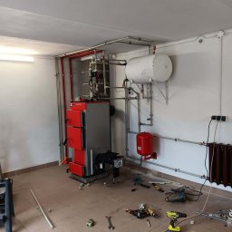MK-INSTAL Michał Kaczmarski - Montaż kotła grzewczego Defro w kotłowni, widoczne narzędzia i instalacja hydrauliczna w trakcie podłączania.