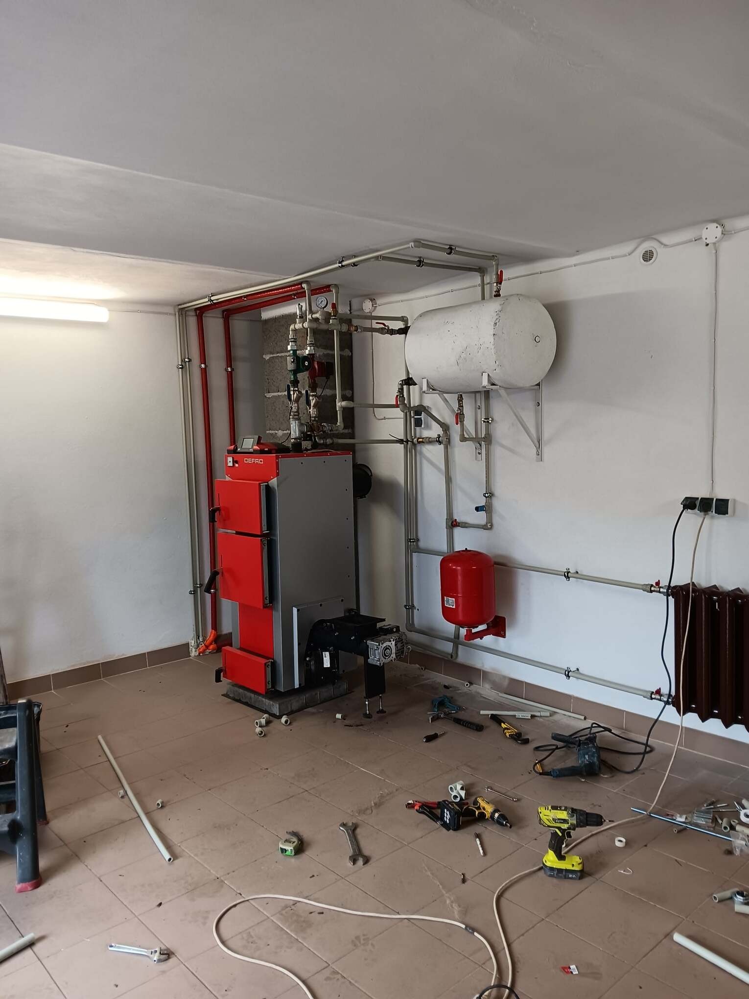 Montaż kotła grzewczego Defro w kotłowni, widoczne narzędzia i instalacja hydrauliczna w trakcie podłączania.