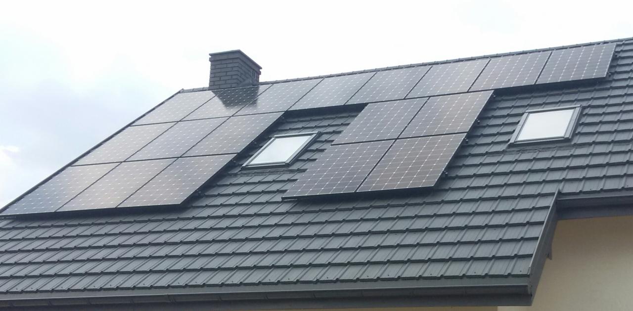 Panele słoneczne na grafitowym dachu domu jednorodzinnego z oknami dachowymi i kominem w tle, widok z dołu.