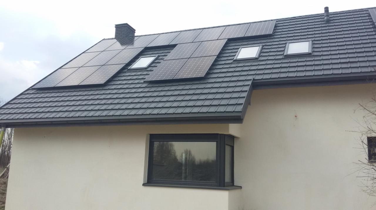 Panele słoneczne na dachu domu z szarą dachówką i oknami dachowymi oraz oknem narożnym na elewacji.